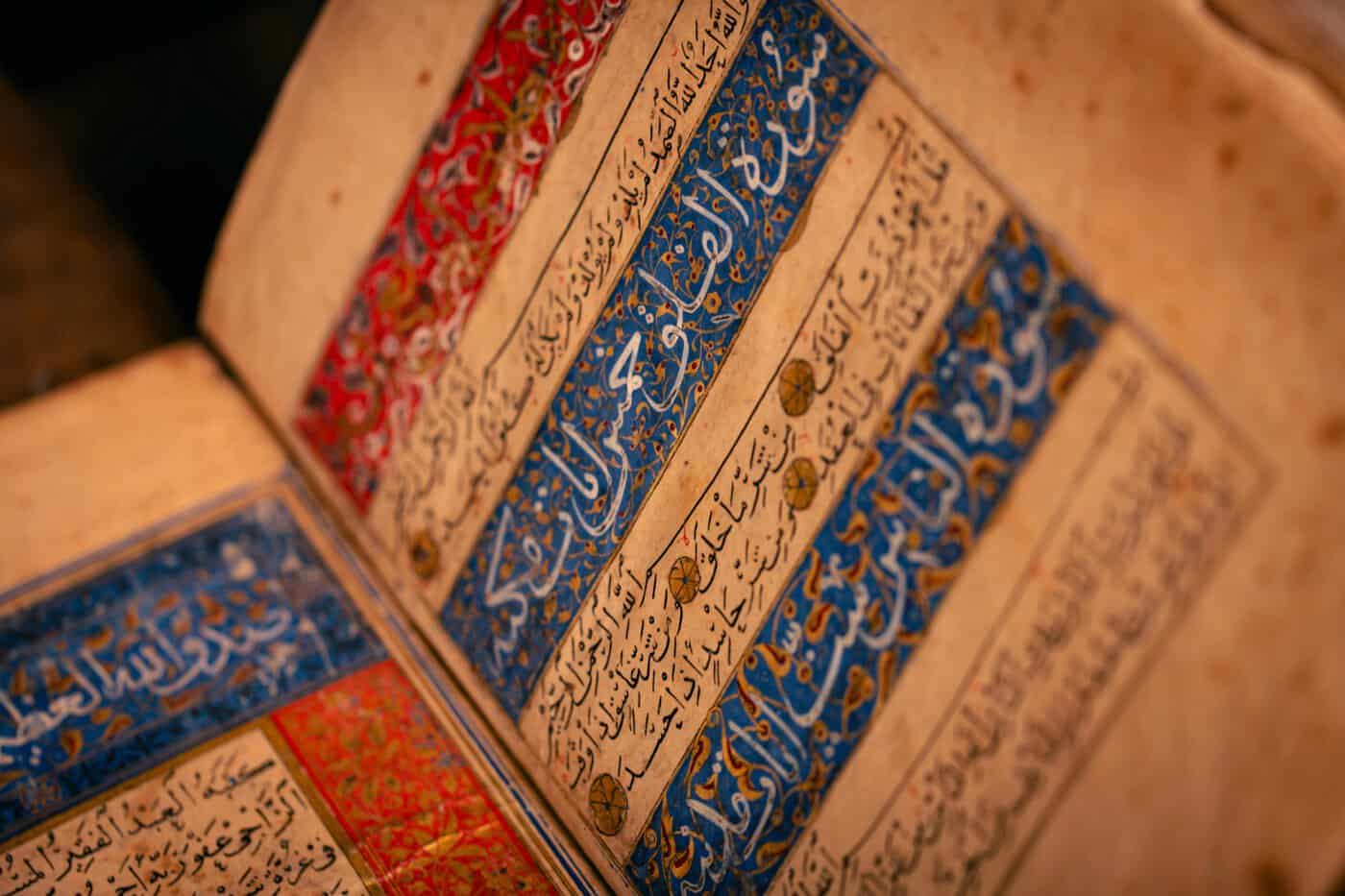 Close-up of an ancient illuminated Islamic manuscript with intricate red, blue, and gold Arabic calligraphy and decorative borders