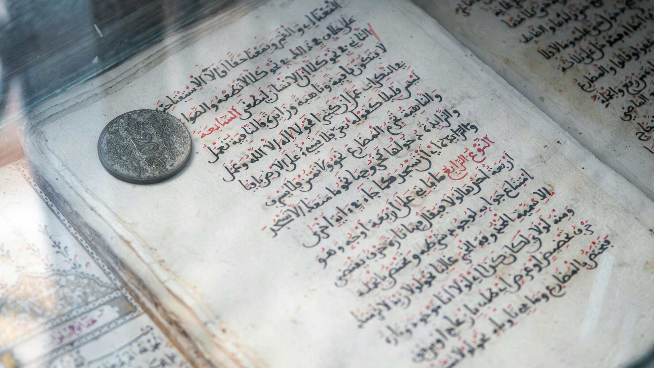 Old handwritten Arabic manuscript with red and black ink under a glass display