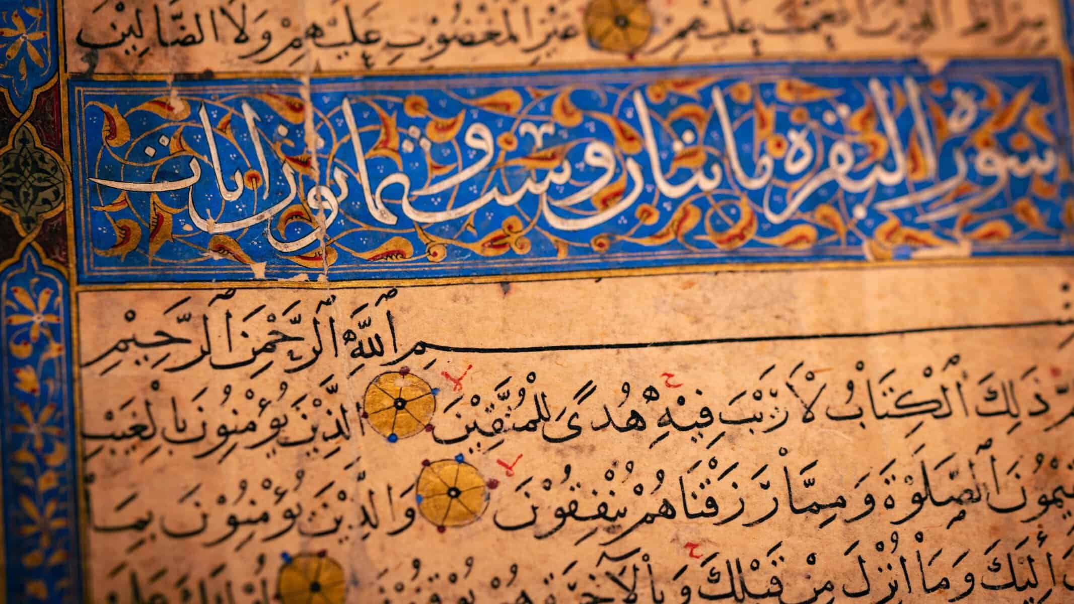 Close-up of an illuminated Quranic page showing Surah Al-Baqarah header in gold and blue
