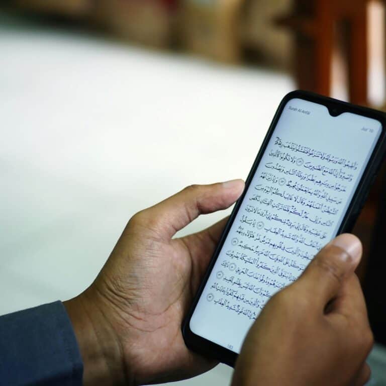 Hands holding a smartphone displaying the Quran in Arabic inside a mosque