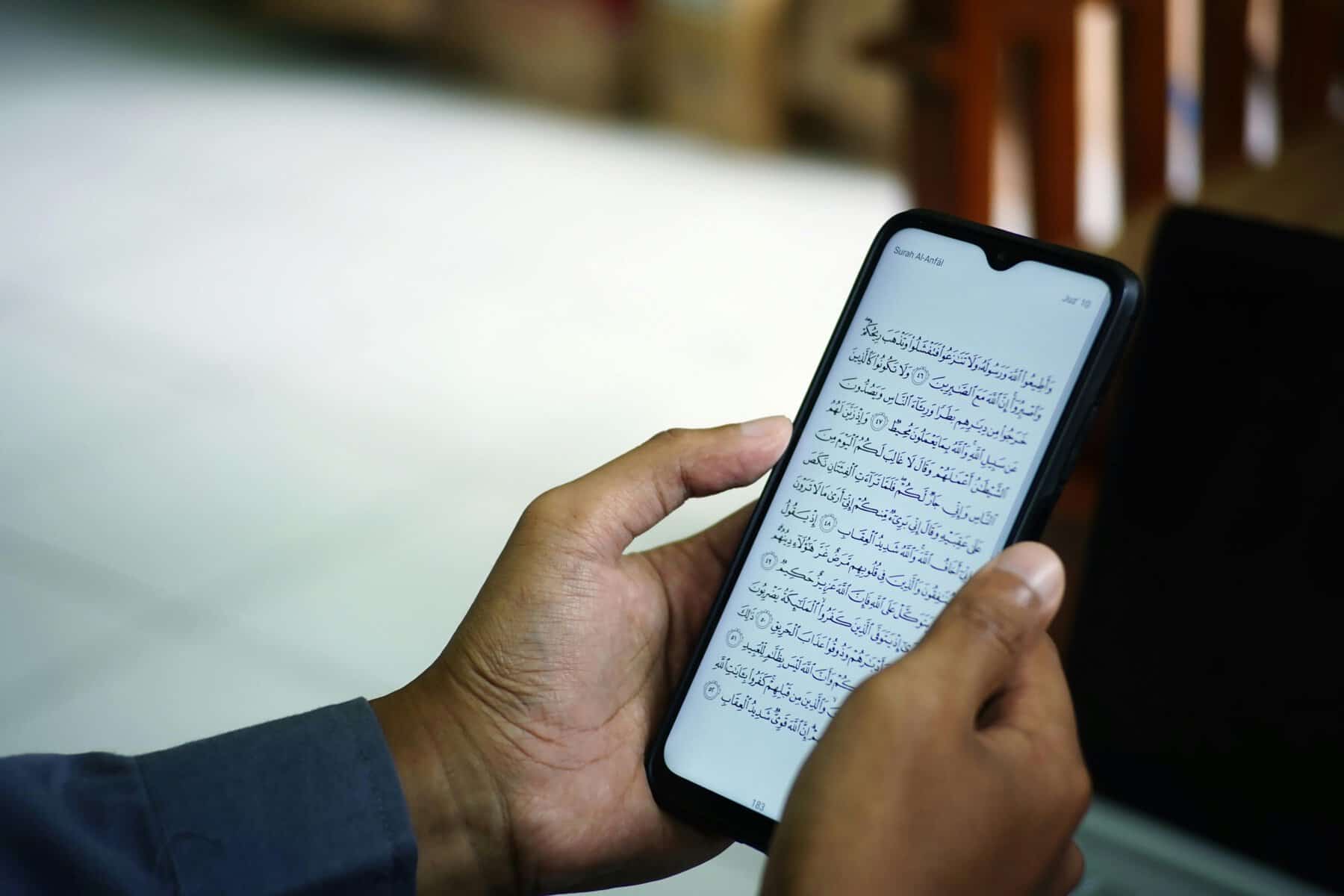 Hands holding a smartphone displaying the Quran in Arabic inside a mosque