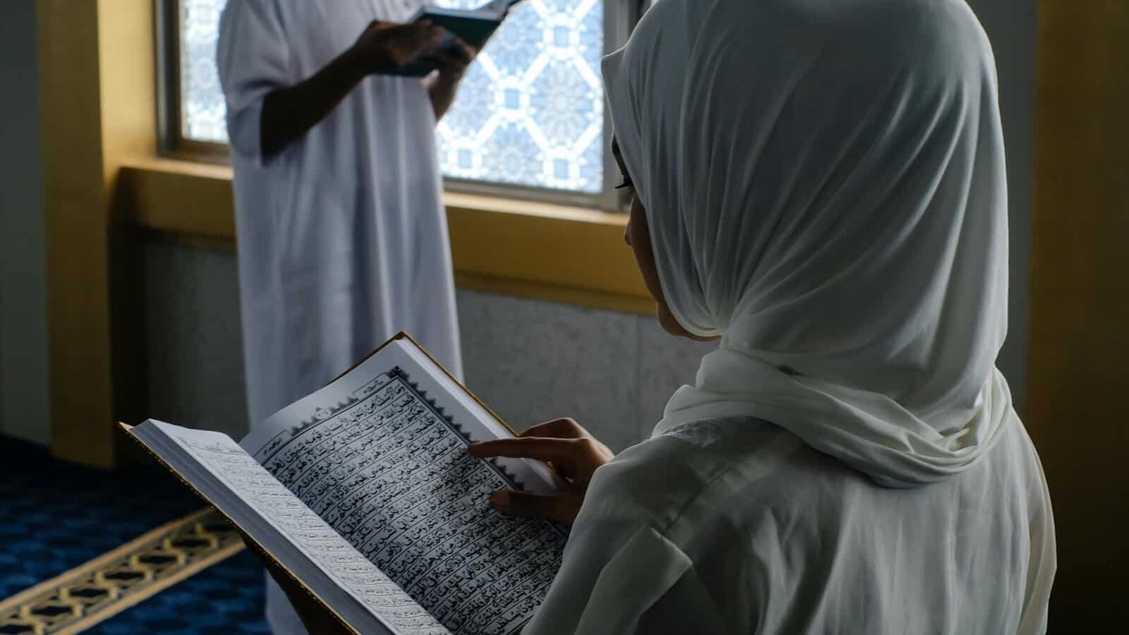 Two Muslim students reading and memorising the Quran beside a large mosque window