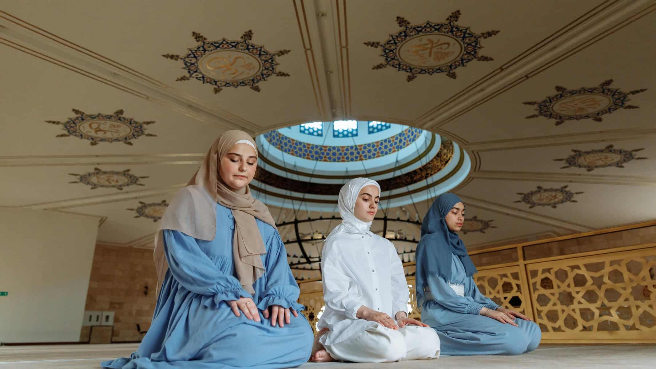 Three Muslim women sitting in quiet contemplation under a mosque dome