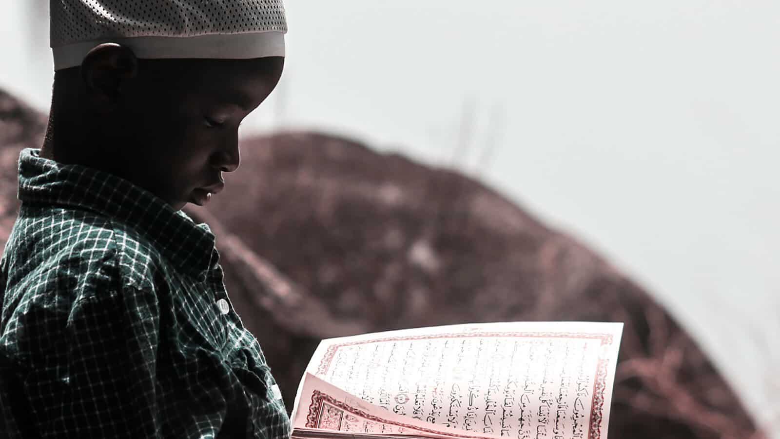 Young Muslim boy reading the Quran outdoors