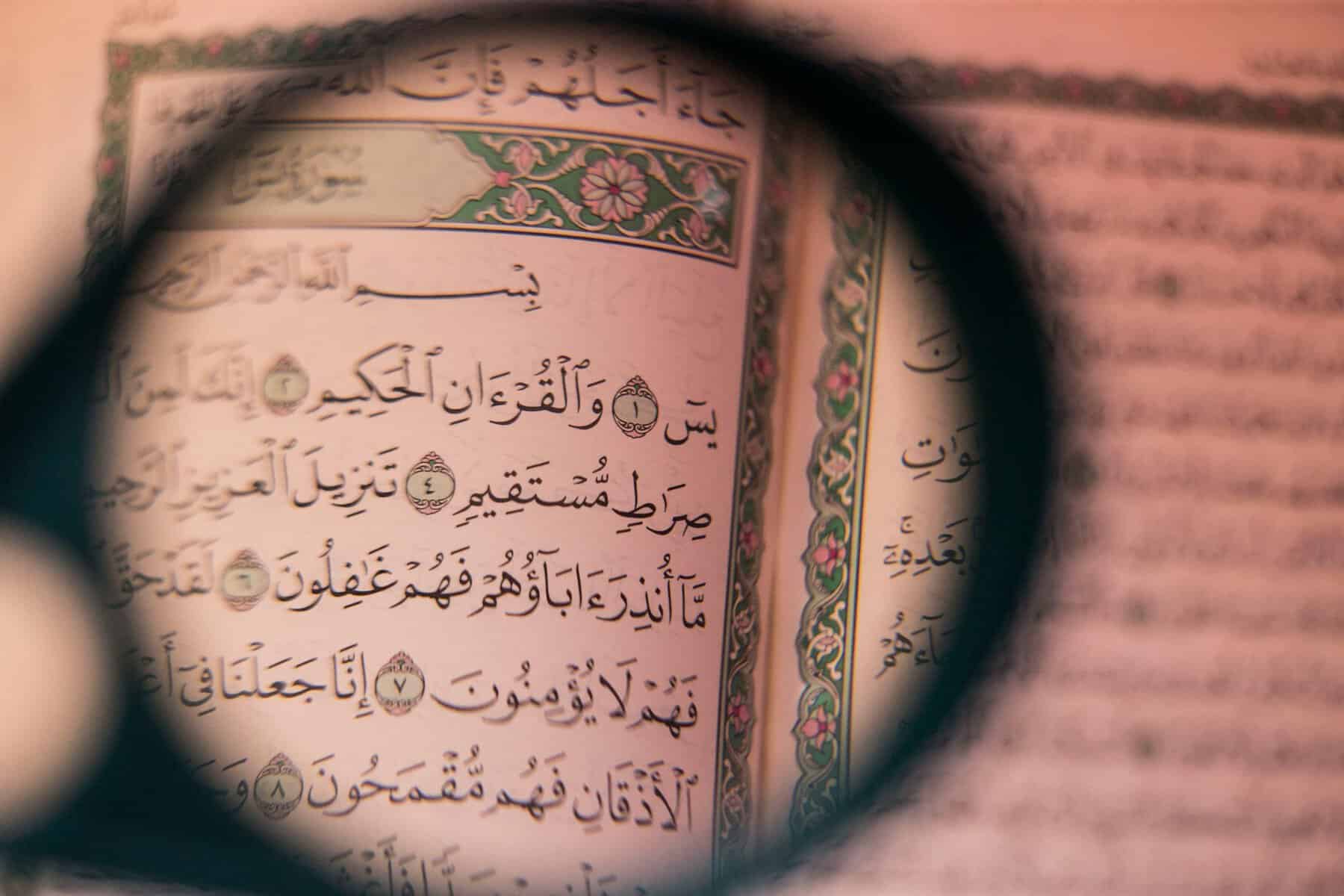 Magnifying glass over an open Mushaf showing real Arabic text from Surah Yaseen, illustrating the depth of seeking knowledge in Islam