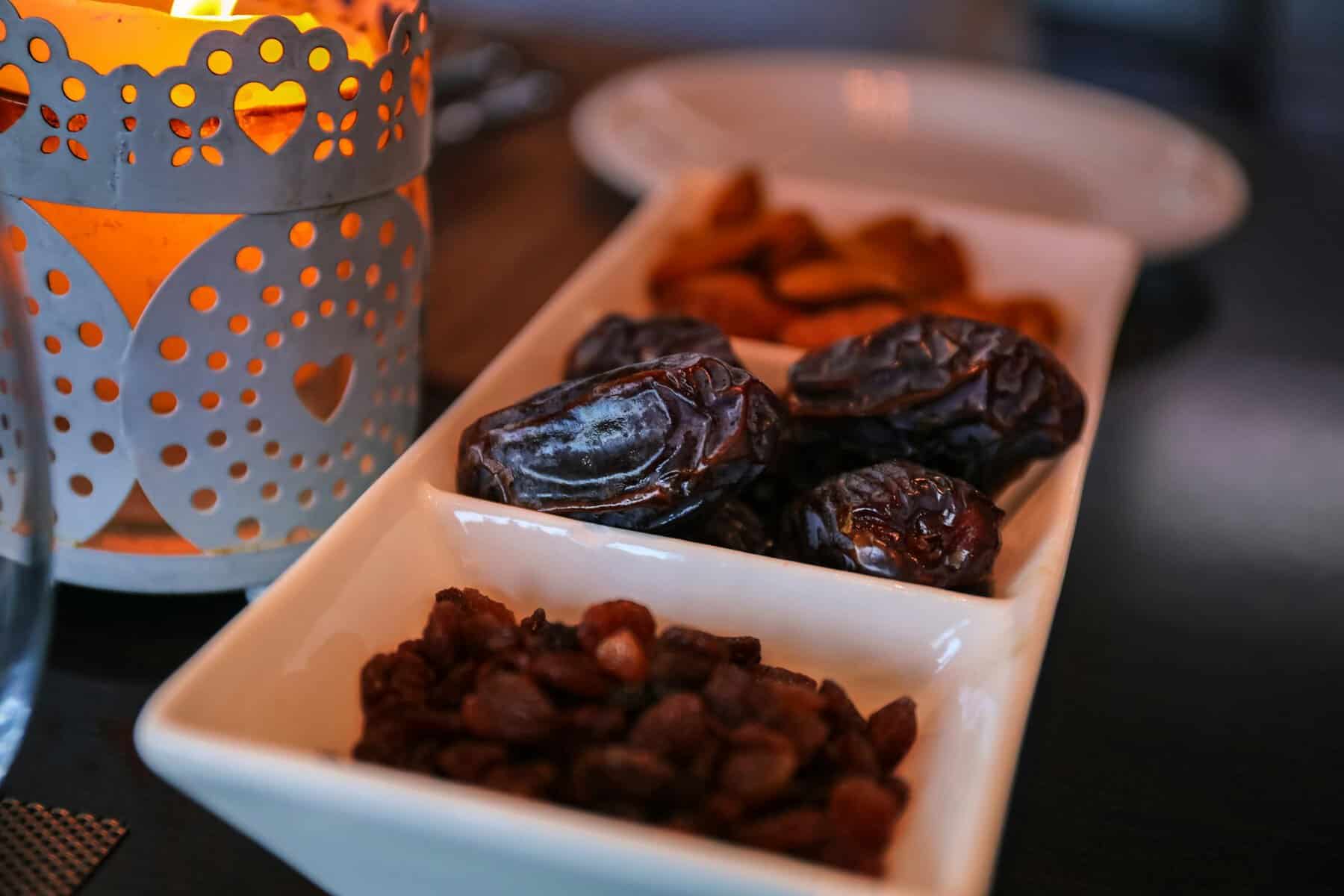 Warm Ramadan iftar setting with medjool dates almonds and raisins beside a lit decorative lantern