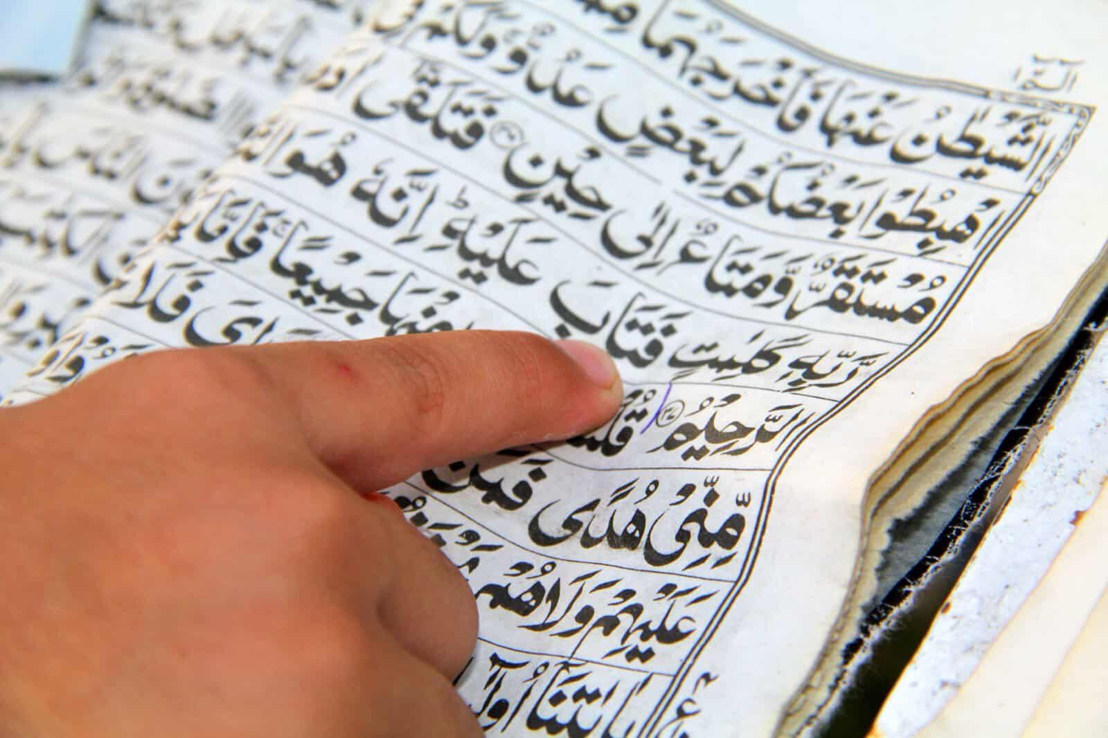 A finger tracing the Arabic words of an open Qur'an, the basic skill taught in online reading lessons