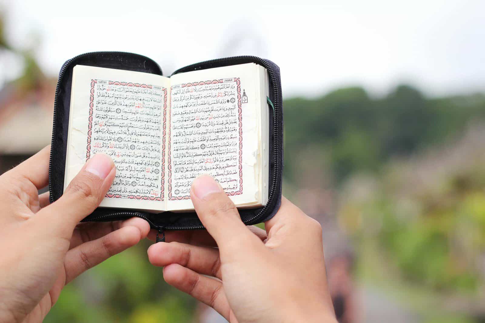 A pair of hands holding an open Quran outdoors, carrying its guidance into everyday life