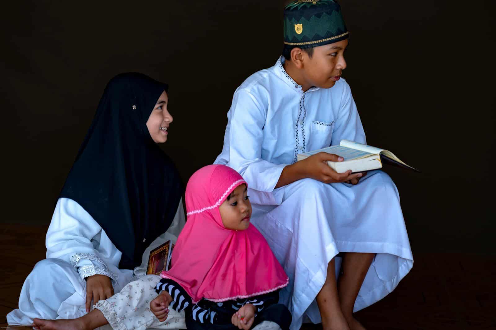 Three Muslim children learning to read the Quran together, one reciting aloud