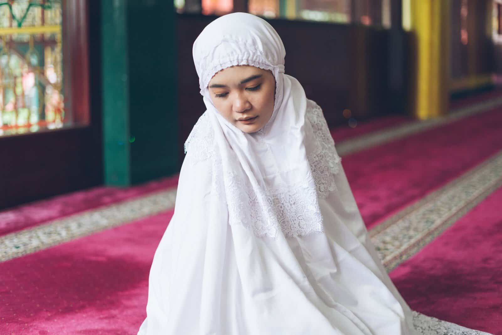 A Muslim woman in modest white dress praying in a mosque, an example of modest covering