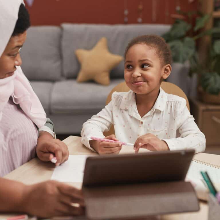 A Muslim mother and her young daughter learning together at home with a tablet