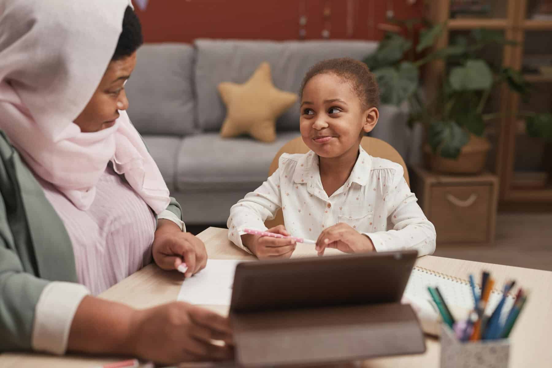 A Muslim mother and her young daughter learning together at home with a tablet