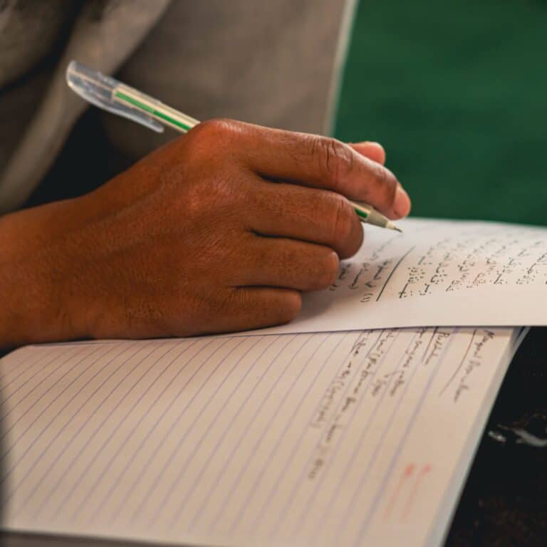 A hand writing Arabic script in a notebook while learning Arabic for the Quran