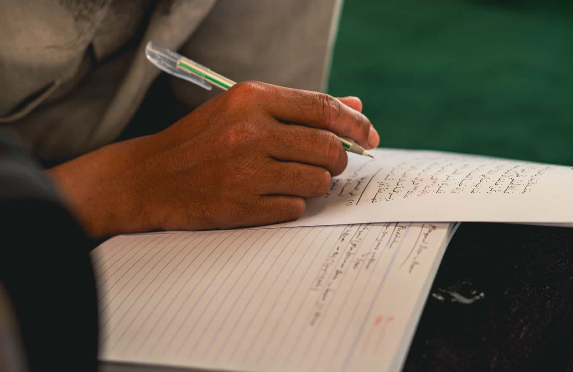 A hand writing Arabic script in a notebook while learning Arabic for the Quran