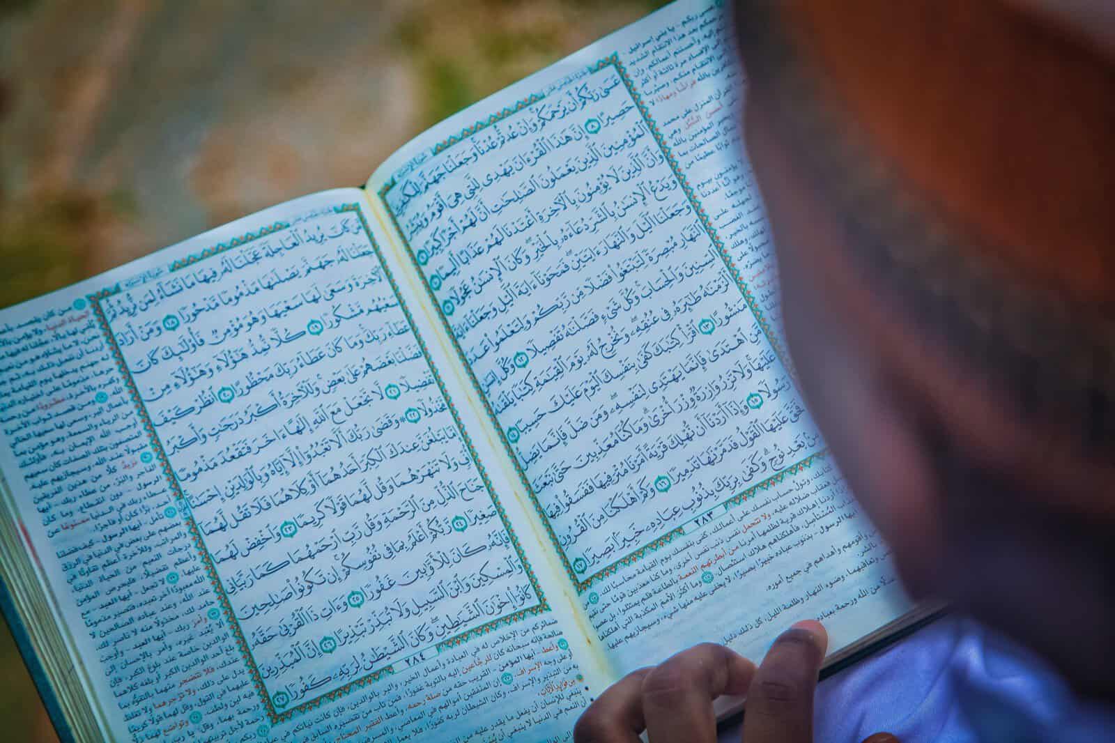 A person reading an open Quran in natural light, tracing the verses