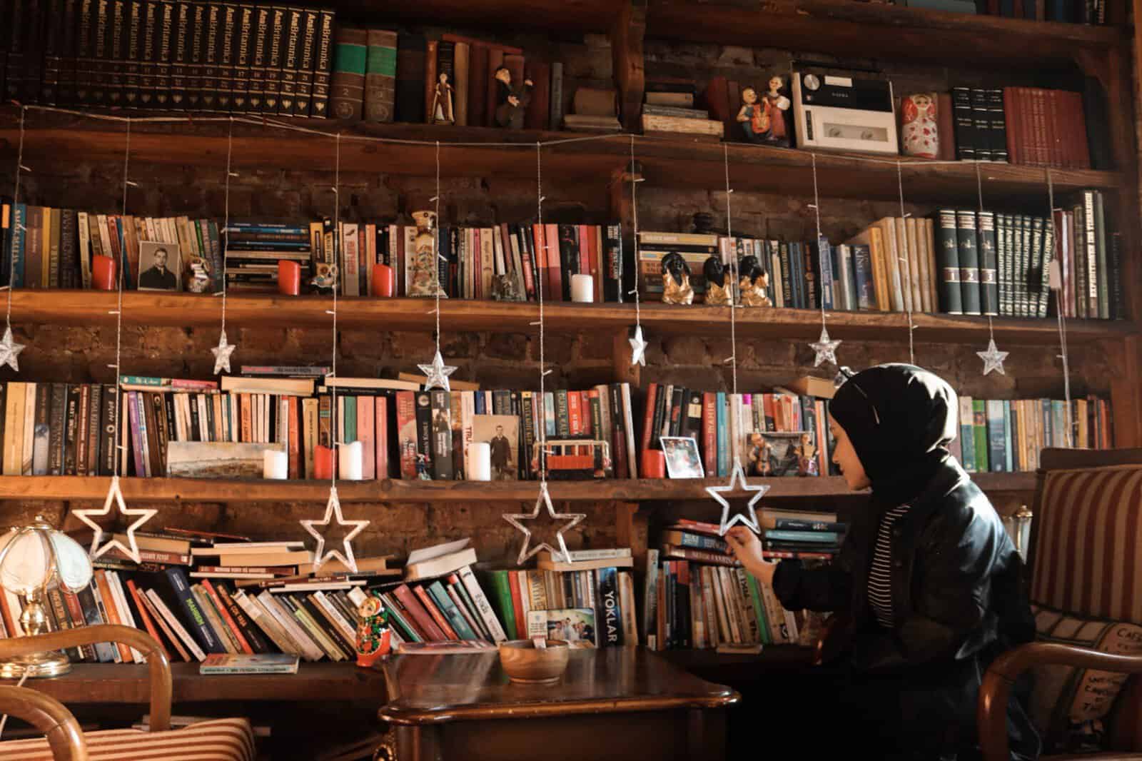 A woman in hijab studying among bookshelves in a library, seeking Islamic knowledge