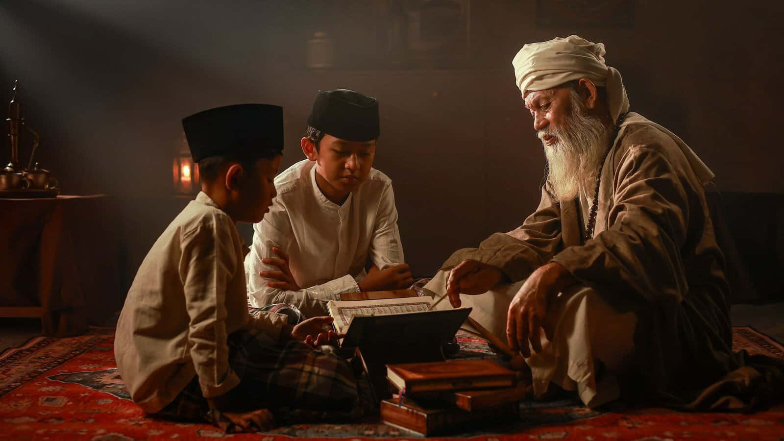 An elderly teacher pointing at the text of a Mushaf while two young students follow along