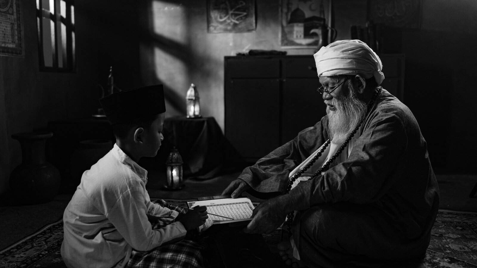 An elderly Quran teacher and a young boy reciting together from an open Mushaf, illustrating the one-to-one transmission behind an ijazah