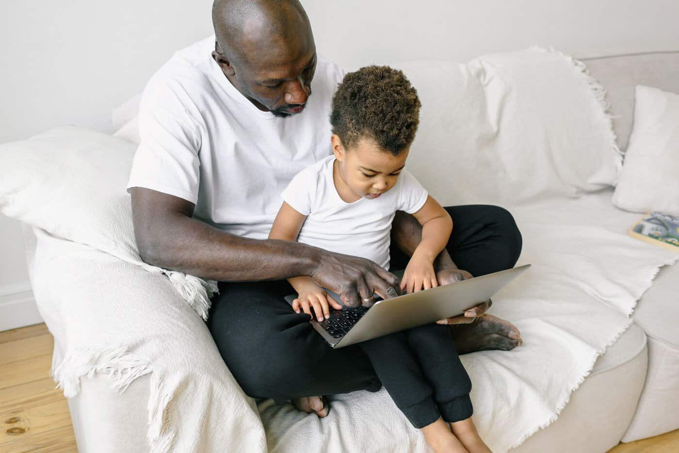 A father and his young son sitting on a sofa looking at a laptop together