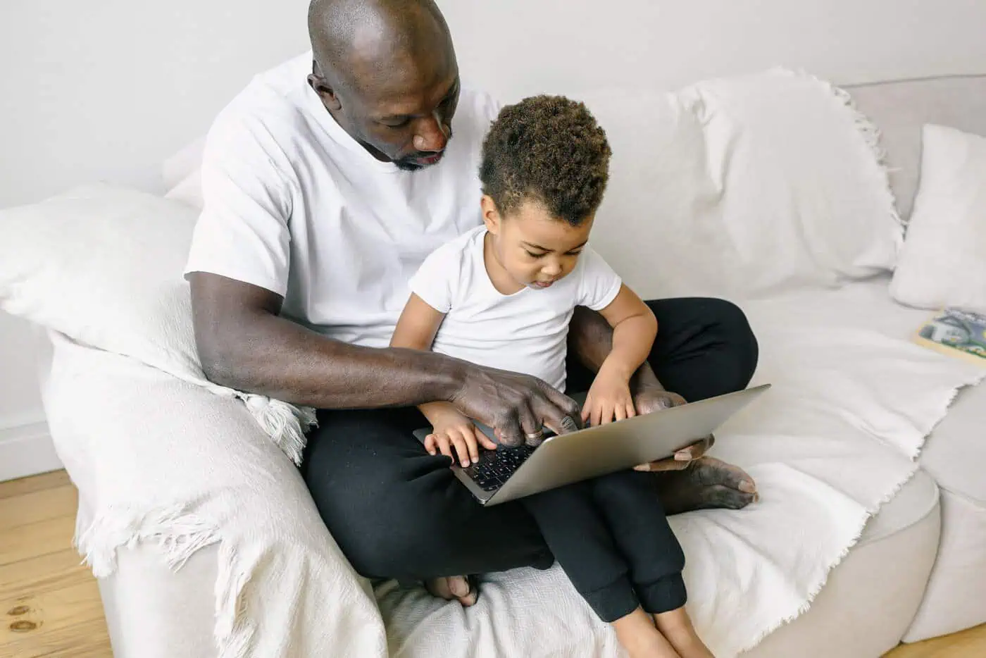A father and his young son sitting on a sofa looking at a laptop together