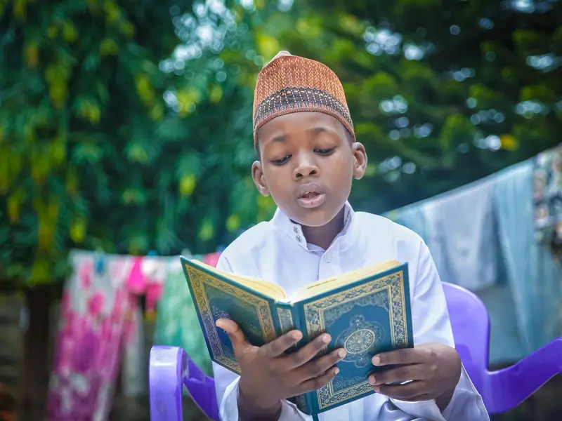 A boy in a kufi reciting aloud from the Quran