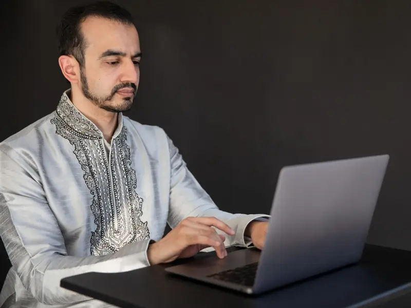 A man in an embroidered kurta studying at a laptop