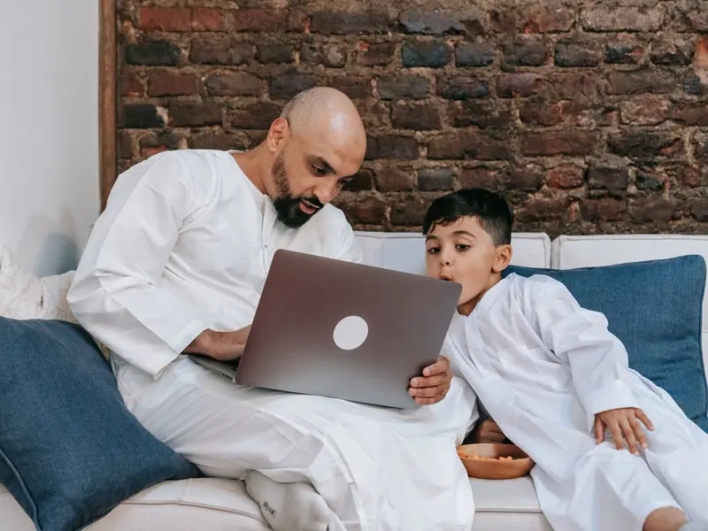 A father and son on a sofa learning together on a laptop